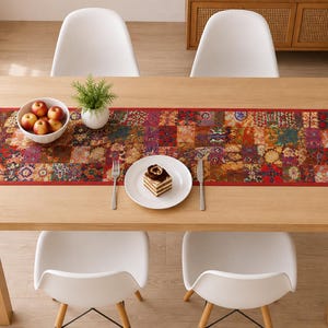 Op de afbeelding: Een rechthoekige tafelloper met een levendig patchworkontwerp met ingewikkelde bloemen- en geometrische patronen in tinten rood, oranje, geel en blauw, afgewerkt met een effen rode rand, weergegeven op een lichthouten eettafel.