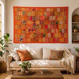 May include: A rectangular wall hanging featuring a patchwork design of various orange, red, and gold fabric squares. The textile displays intricate floral and geometric patterns with embroidered details, all framed by a solid orange fabric border.