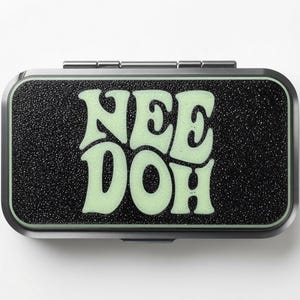 May include: A rectangular metal tin with a hinged lid featuring a textured black surface and the word NEE DOH printed in large, pale green, rounded letters. The container has a metallic silver frame and a smooth, rounded edge design.