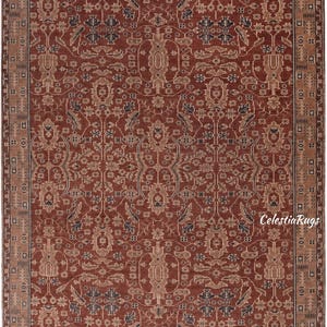 May include: A rectangular area rug featuring a deep terracotta red background with intricate floral and geometric patterns in shades of beige, tan, and dark charcoal. The rug has a wide decorative border and short fringe at the top and bottom edges.