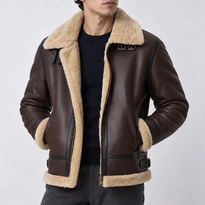May include: A dark brown leather jacket featuring a thick beige shearling lining, a wide fold-over collar, a front zipper closure, and adjustable buckle straps at the collar and waist. The jacket has long sleeves with shearling cuffs.