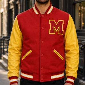 May include: A red varsity jacket with yellow sleeves, featuring a large yellow letter M on the left chest. The jacket has a snap-button front closure, two side pockets with yellow trim, and striped ribbed cuffs and collar in red, white, and yellow.