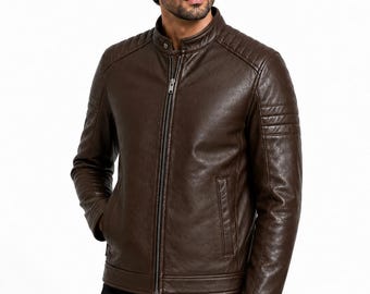 Puede incluir: Una chaqueta de cuero marrón oscuro con cuello alzado y cierre de botón a presión, cremallera frontal completa y detalles acolchados en los hombros y la parte superior de las mangas. La chaqueta incluye dos bolsillos laterales.