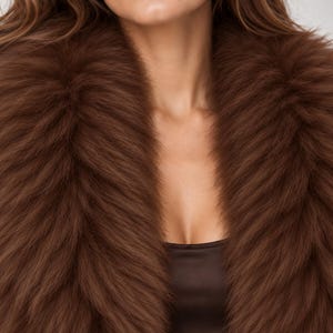 May include: A thick, plush brown faux fur collar draped around the neck and shoulders. The collar features long, dense, textured fibers in a deep chocolate brown shade, creating a voluminous and layered appearance over a dark brown top.