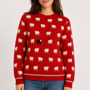 May include: A long-sleeved red crewneck sweater featuring a repeating pattern of small, off-white sheep. One single black sheep is positioned in the center of the chest area. The sweater has a ribbed knit collar, cuffs, and a hem with a small pattern.