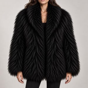 May include: A black faux fur jacket featuring a long-pile texture with a distinct chevron-like pattern throughout the fabric. The garment has a wide, voluminous shawl collar and long sleeves, with an open front design that falls to the hips.