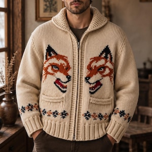 May include: A beige knit zip-up cardigan featuring a shawl collar and two front pockets. The garment displays a prominent orange, black, and white fox head graphic on each side of the chest, with a small geometric pattern along the bottom hem.