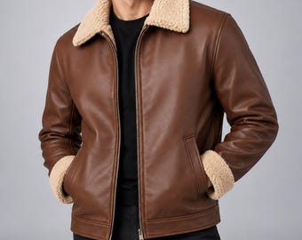 Puede incluir: Una chaqueta de cuero marrón con cuello de sherpa beige y puños de sherpa a juego en las muñecas. La chaqueta tiene un cierre de cremallera frontal completo, dos bolsillos laterales y se lleva sobre una camiseta negra y pantalones negros.
