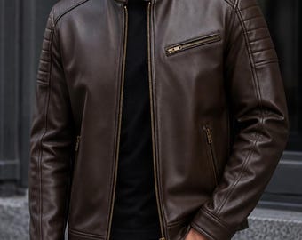 Puede incluir: Una chaqueta de cuero marrón oscuro con cuello alzado y cierre de botón a presión, cremallera frontal completa y detalles acolchados acanalados en los hombros. La chaqueta incluye un bolsillo en el pecho con cremallera y dos bolsillos laterales.