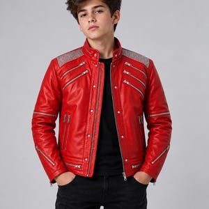 May include: A vibrant red leather jacket featuring a stand-up collar, silver-toned metal zippers on the chest and sleeves, and ribbed shoulder panels. The jacket is worn over a plain black t-shirt and paired with black denim jeans.