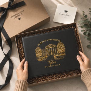 May include: A black leather-like photo album in a gift box with a gold foil print of Purdue University, the name Tyler, and the text Class of 2025. The box lid features the text Congratulations Graduate with a graduation cap icon and a black ribbon.