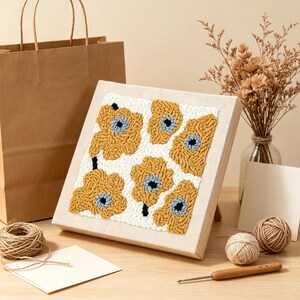 May include: A square punch needle embroidery art piece on a wooden frame featuring a repeating floral pattern with mustard yellow petals, light blue centres, and a white background. The text MossPunchCraft is printed at the bottom of the image.