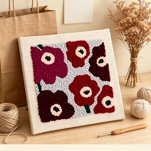 May include: A square punch needle embroidery art piece on canvas featuring a floral pattern with large, stylised flowers in shades of deep red, burgundy, and magenta with pale pink centres, set against a light grey background. Text reads MossPunchCraft.