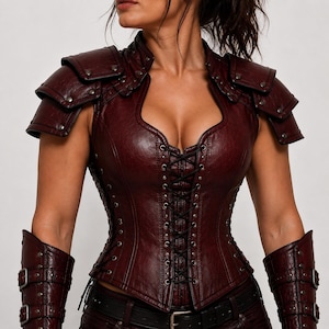 May include: A dark burgundy faux leather corset top featuring layered shoulder pauldrons with metal studs, a front lace-up closure with black cord, and matching forearm bracers with buckle straps. The garment has a textured finish and metal eyelets.