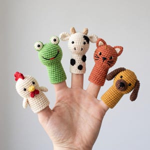 May include: A set of five crocheted finger puppets featuring a white chicken with a red comb, a green frog, a white cow with black spots, an orange cat with whiskers, and a brown dog with floppy ears, each crafted with detailed yarn stitching.