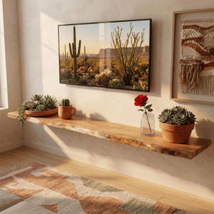 Könnte beinhalten: Ein langes, wandmontiertes Schweberegal aus Holz mit Naturkante, auf dem eine Terrakottaschale mit Sukkulenten, ein kleiner Kaktus in einem Becher, eine einzelne rote Rose in einem Glasgefäß und eine Sukkulente im Topf unter einem Fernseher stehen.