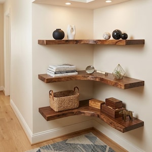 May include: Three L-shaped floating shelves made of dark brown wood with natural live edges. The shelves hold various decorative items including a black vase, a white sculpture, books, a magnifying glass, a woven basket, and wooden boxes.