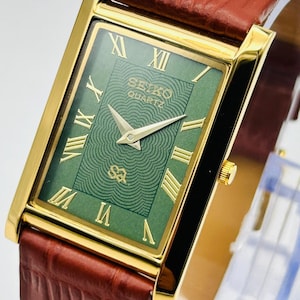 May include: A rectangular Seiko Quartz wristwatch featuring a gold-tone case, a green dial with a concentric wave pattern, and gold Roman numeral hour markers. The watch includes gold hands and a brown leather strap with a textured crocodile-style finish.