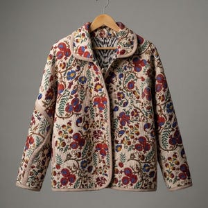 Op de afbeelding: Een gewatteerd jack in een lichtbeige tint met een levendige, meerkleurige bloemen- en botanische print in rood-, blauw- en groentinten. Het kledingstuk heeft een ronde kraag, lange mouwen en een rechte zoom, afgewerkt met lichtroze biezen.