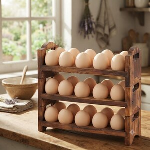 May include: A dark brown wooden egg storage rack with three horizontal shelves, each holding a row of light beige eggs. The rack features arched side supports with integrated handle cutouts, providing a structured display for the eggs.