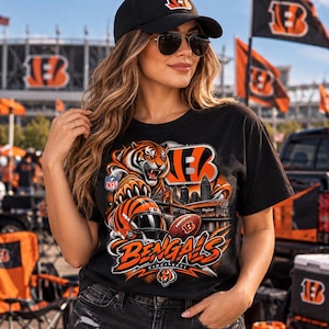 May include: A black short-sleeve t-shirt featuring a graphic print of a roaring tiger, a football helmet, a football, and the Cincinnati Bengals team logo. The design includes the text Bengals and Cincinnati with an NFL shield emblem.