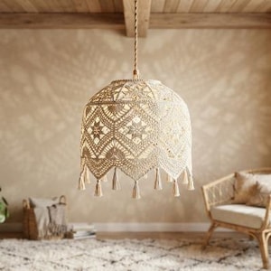 Puede incluir: Una lámpara colgante de macramé beige con un intrincado patrón de nudos, una pantalla en forma de cúpula y borlas decorativas que cuelgan del borde inferior, suspendida de un cable trenzado sujeto a una viga de madera.