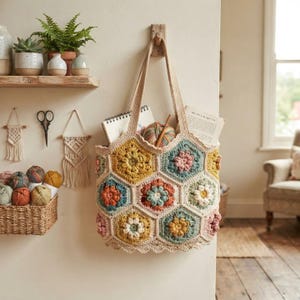 Peut inclure: Un sac fourre-tout en crochet composé de motifs hexagonaux multicolores avec des centres floraux dans des tons jaune moutarde, vert sauge, rose poudré et terre cuite. Le sac possède deux anses solides et contient un carnet et de la laine.