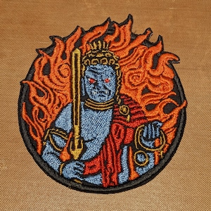 Puede incluir: Parche bordado con una deidad azul con ojos rojos, sosteniendo una espada dorada, rodeada de llamas naranjas. La deidad lleva una túnica roja y dorada.