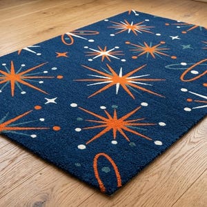 Könnte beinhalten: Ein rechteckiger Teppich mit tiefblauem Hintergrund und einem sich wiederholenden Muster aus orangefarbenen und weißen Sternen, kleinen Punkten und elliptischen Formen. Die Designelemente sind in einer geometrischen Anordnung verteilt.