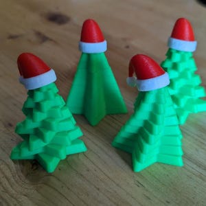 May include: Four small, green, tiered, star-shaped figurines resembling Christmas trees. Each figurine is topped with a miniature red Santa hat featuring a white brim. The objects have a smooth, matte finish and a distinct geometric, layered structure.