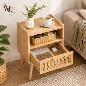 May include: A light wood nightstand with a top shelf and one pull-out drawer. The drawer front features a woven cane panel. On the top shelf sits a white ceramic mug and a small white vase with greenery. Inside the drawer is a magazine titled Cereal.