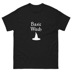 May include: A black short-sleeved t-shirt featuring the white text "Basic Witch" printed on the center of the chest, positioned directly above a simple white graphic illustration of a pointed witch hat with a wide brim.
