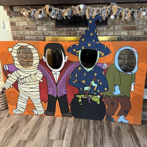 May include: A large rectangular Halloween photo cutout board featuring four characters: a mummy wrapped in beige bandages, a vampire in a purple suit, a witch in a blue star-patterned hat stirring a black cauldron, and a blue-skinned zombie.