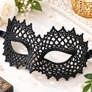 May include: A black lace masquerade mask featuring an intricate, knotted, open-work pattern with a scalloped edge. The mask has two eye openings and is secured with black satin ribbons on each side, showcasing a detailed, textured, and woven design.