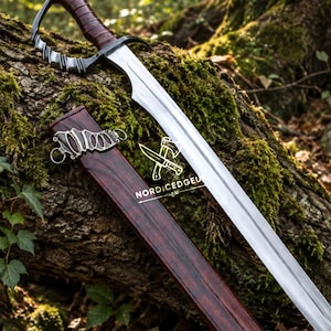 May include: A steel sword with a curved blade and a dark brown leather-wrapped handle featuring a silver metal guard. The sword is accompanied by a matching dark brown wooden scabbard with a silver metal fitting. The text NORDICEDGELOGO is visible.