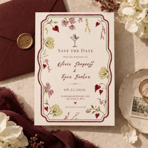 Op de afbeelding: Een crèmekleurige Save the Date-kaart met een donkerrode rand, aquarelillustraties van bloemen en harten, en een martiniglas-icoon. De tekst luidt: Save the Date for the wedding of Olivia Sergeeff & Ryan Boshan 08.22.2026.