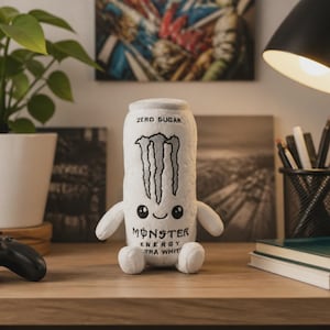 Op de afbeelding: Een wit pluche speelgoed in de vorm van een Monster Energy Ultra White drankblikje. Het pluche heeft het zwarte Monster-logo, de tekst "ZERO SUGAR" en "MONSTER ENERGY ULTRA WHITE", en een schattig geborduurd gezichtje met twee zwarte ogen.