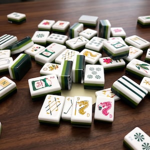May include: A collection of rectangular mahjong tiles scattered across a surface. The tiles are white with dark green backs and feature various colourful illustrations, including dragons, golf clubs, flowers, and numbers in black, green, red, and gold.