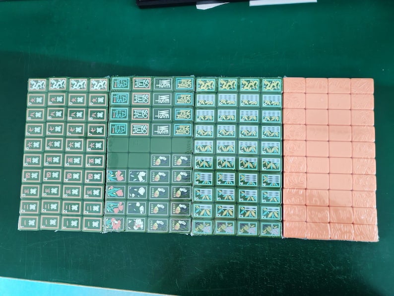 May include: A set of rectangular mahjong tiles arranged in four columns. Three columns feature green tiles with various engraved symbols, Chinese characters, and floral patterns. The fourth column consists of plain, solid peach-colored tiles.
