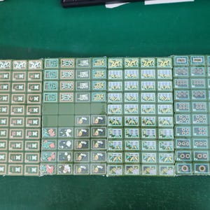 May include: A complete set of green mahjong tiles arranged in four rectangular blocks. The tiles feature various traditional Chinese characters, bamboo patterns, circular symbols, dragon motifs, wind directions, and flower illustrations in white, red, and green.