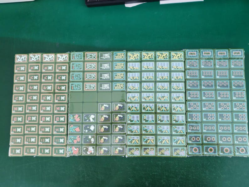 May include: A complete set of green mahjong tiles arranged in four rectangular blocks. The tiles feature various traditional Chinese characters, bamboo patterns, circular symbols, dragon motifs, wind directions, and flower illustrations in white, red, and green.