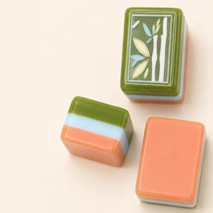 May include: Three rectangular mahjong tiles with smooth, glossy surfaces. One tile features a green bamboo design on a dark green background. The other two tiles show horizontal layers of olive green, light blue, and peach orange colors.