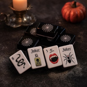 May include: A set of rectangular mahjong tiles featuring Halloween-themed illustrations. The tiles display white faces with black ink graphics including a snake, a potion bottle labeled Joker, a pair of vampire lips, a spider, and spiderwebs.