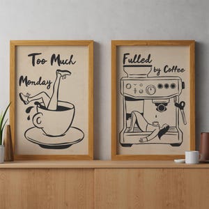 May include: Two framed wall art prints with light beige backgrounds and black line art. The left print shows legs emerging from a coffee cup with the text Too Much Monday. The right print depicts a person lying inside an espresso machine with the text Fueled by Coffee.