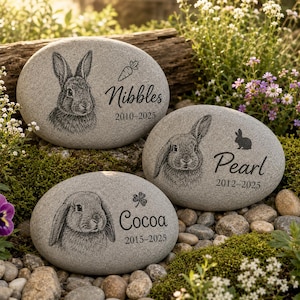May include: Three oval grey memorial stones featuring engraved rabbit portraits and names. The top stone shows a rabbit with a carrot and the name Nibbles 2010-2025. The right stone shows a rabbit with the name Pearl 2012-2025. The bottom stone shows a rabbit with the name Cocoa 2015-2025.