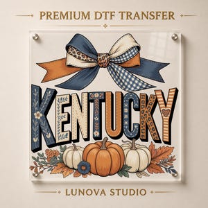 May include: A premium DTF transfer design featuring the word KENTUCKY in block letters with varied patterns including floral, leopard print, and stripes. Above the text is a large bow with blue, cream, and leopard print sections. Below are pumpkins.