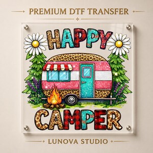 May include: A premium DTF transfer sheet featuring a graphic of a camper trailer with leopard print and pink glitter accents. The text reads HAPPY CAMPER, surrounded by daisies, pine trees, and a campfire. The design is by LUNOVA STUDIO.