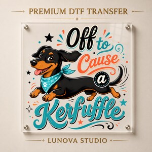 Peut inclure: Un transfert DTF premium représentant un teckel noir et feu portant un bandana bleu clair avec des empreintes de pattes blanches. Le graphique inclut le texte Off to Cause a Kerfuffle en lettres stylisées noires, orange et bleu sarcelle.