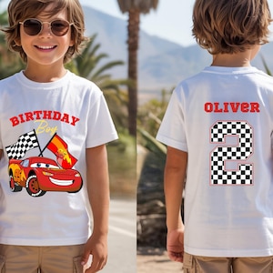 May include: A white t-shirt featuring a red race car graphic with the text "BIRTHDAY Boy" on the front and the name "OLIVER" above a large checkered number "2" on the back. The design includes a checkered flag and a red flag with a lightning bolt.