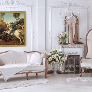 Puede incluir: Un cuadro rectangular enmarcado que representa a un caballero sobre un caballo blanco luchando contra una criatura oscura, expuesto en una pared blanca sobre un sofá color crema. La obra tiene un marco dorado y un paisaje con árboles.